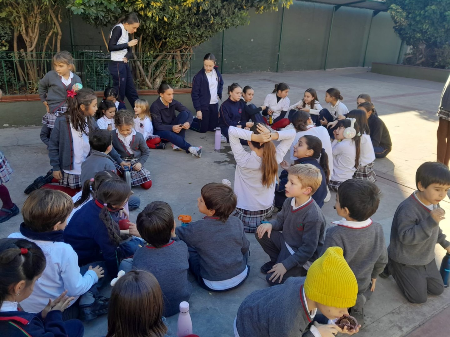 Alumnos de séptimo grado acompañando a los de primer grado sentados en ronda en el patio, proyecto de padrinazgo
