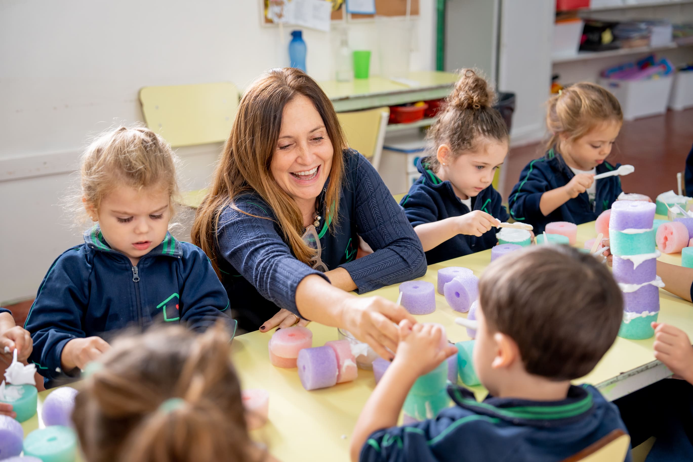 Maestra ayudando a los nenes en una actividad sensorial con espuma de colores en The Green House Kindergarten