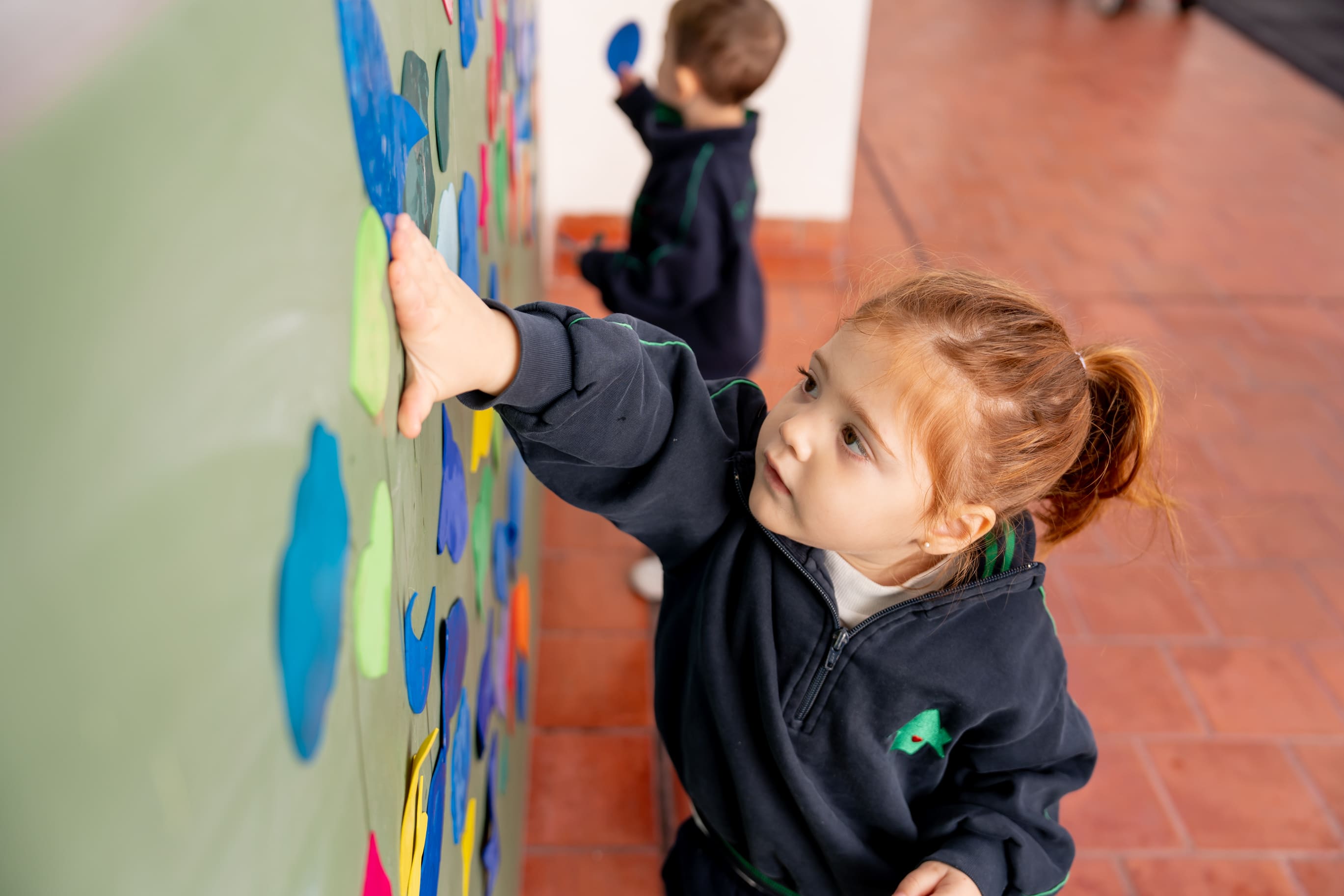 Nena pegando figuras de papel en un mural colaborativo en The Green House Kindergarten