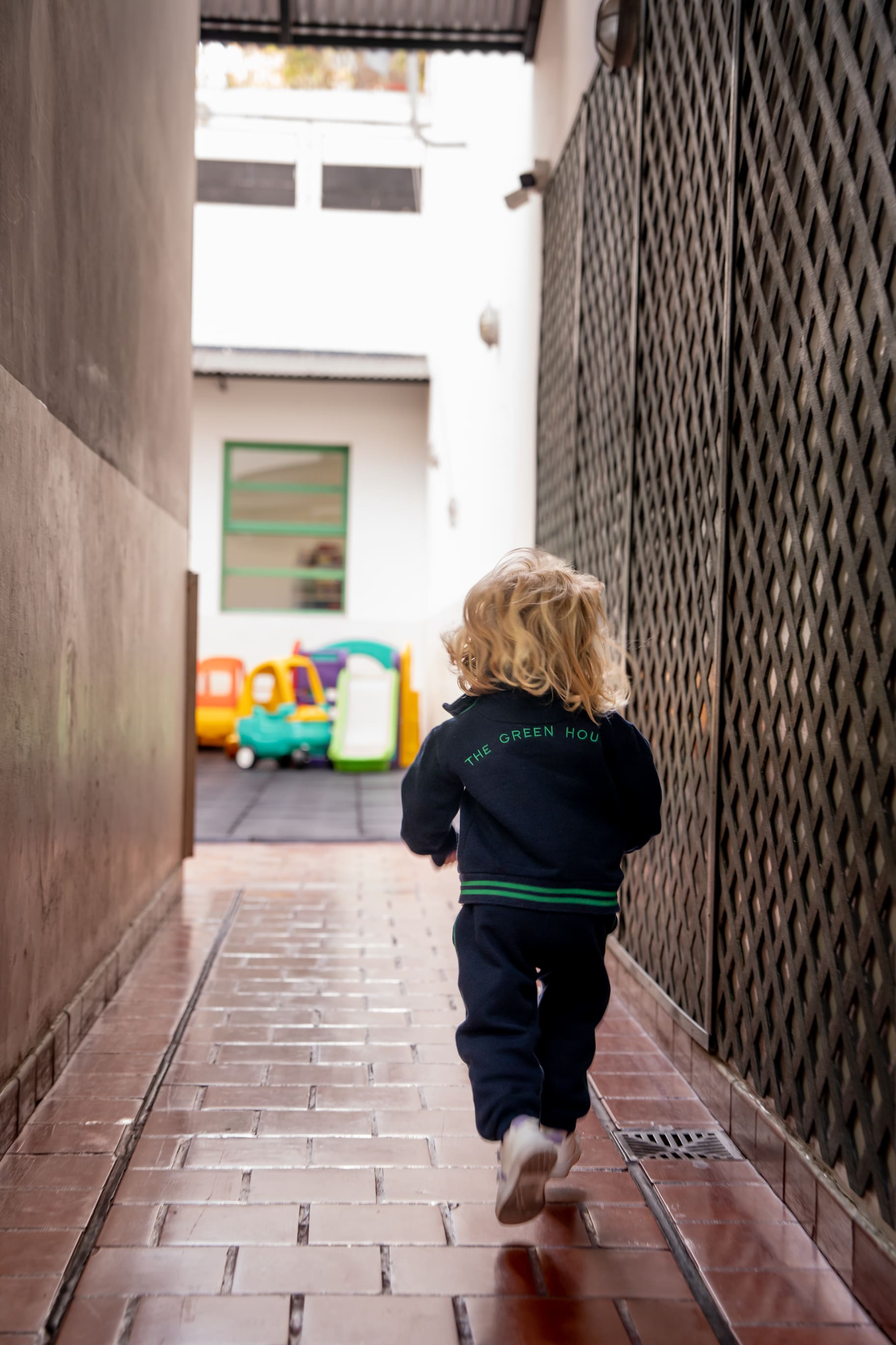 Nene con el buzo de The Green House Kindergarten corriendo hacia los juegos del patio