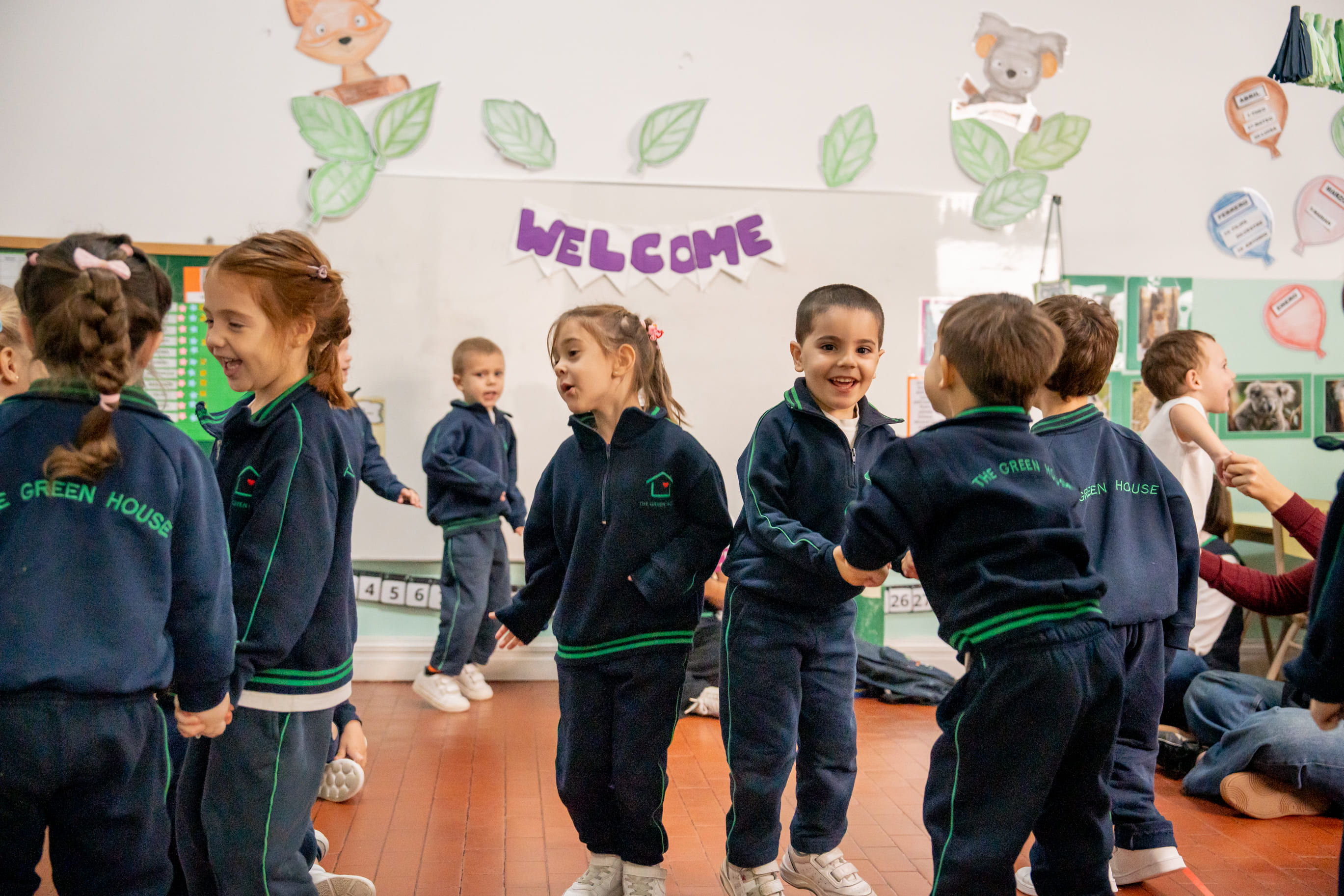 Nenes de The Green House Kindergarten tomados de las manos bailando en ronda en el aula