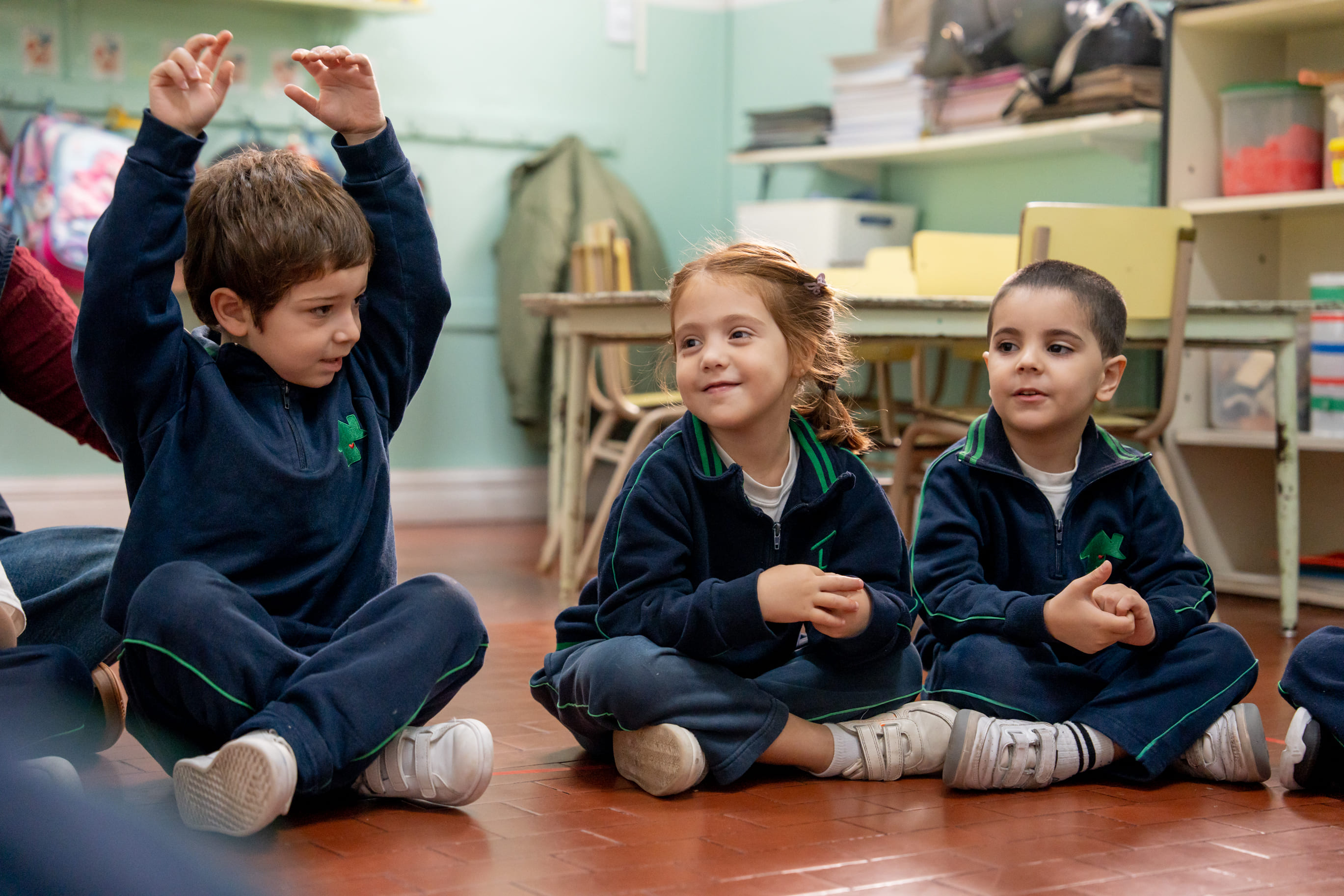 Nenes sentados en el piso del aula cantando con las manos levantadas en The Green House Kindergarten