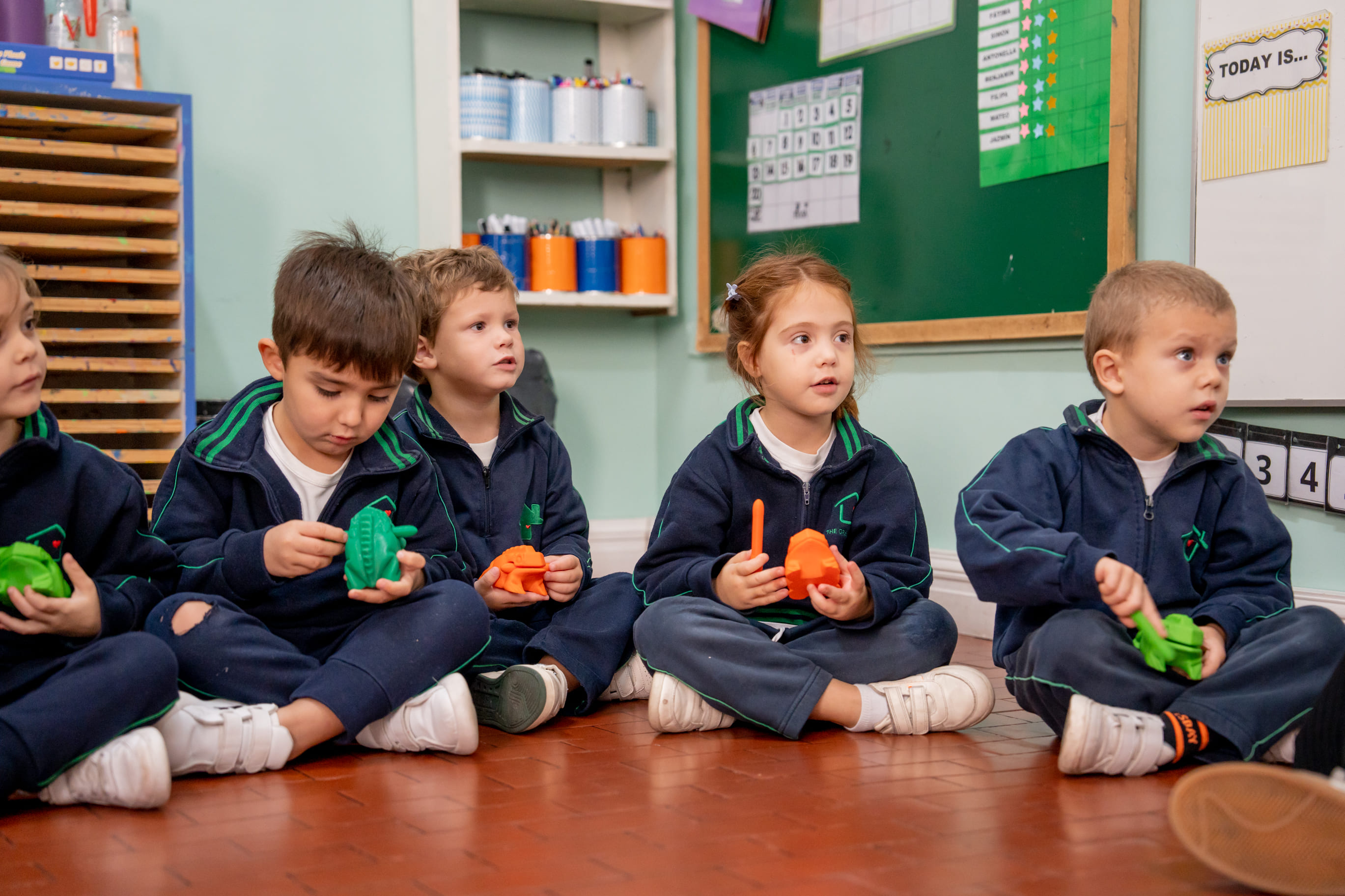 Nenes sentados en el piso del aula jugando con animales de juguete en The Green House Kindergarten