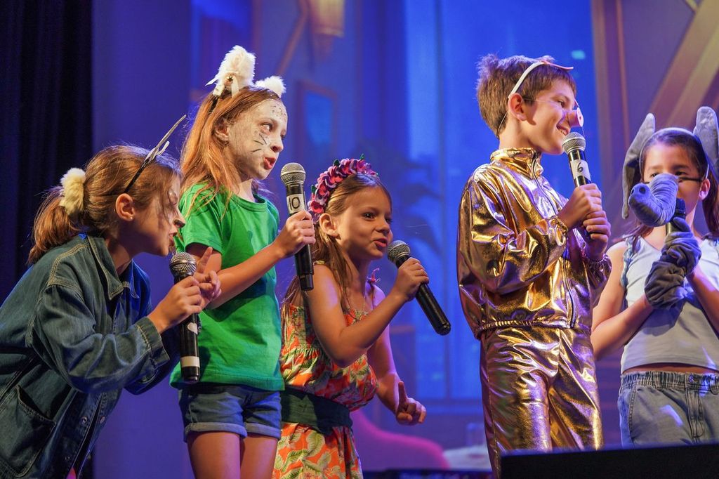 Alumnos de primaria disfrazados cantando con micrófonos en el escenario durante el Concert del Colegio San Javier