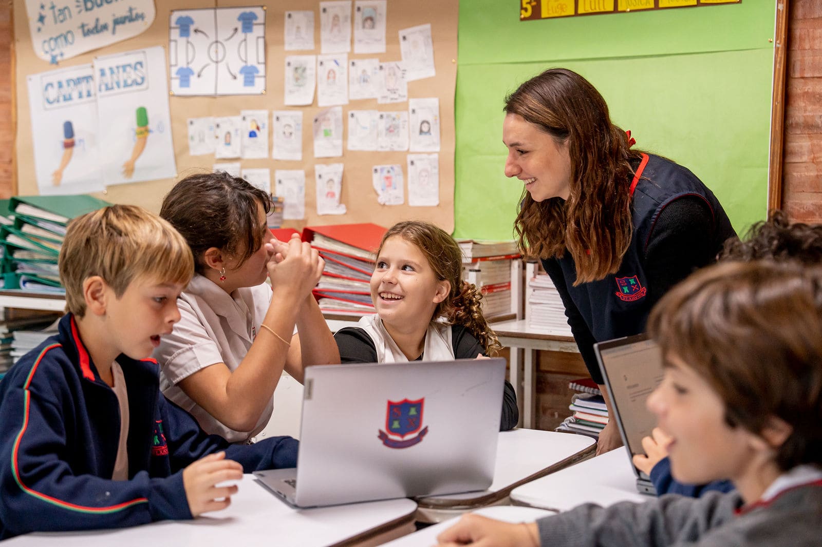 Alumnos de primaria sonriendo junto a su maestra frente a una notebook en el aula del Colegio San Javier